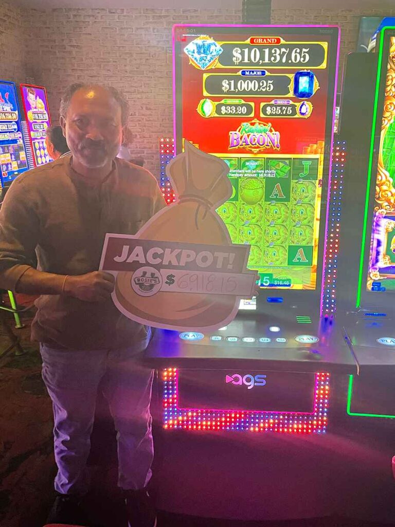 Savy holding a sign on the casino floor that says Jackpot! Rakin Bakin $6,918.15.